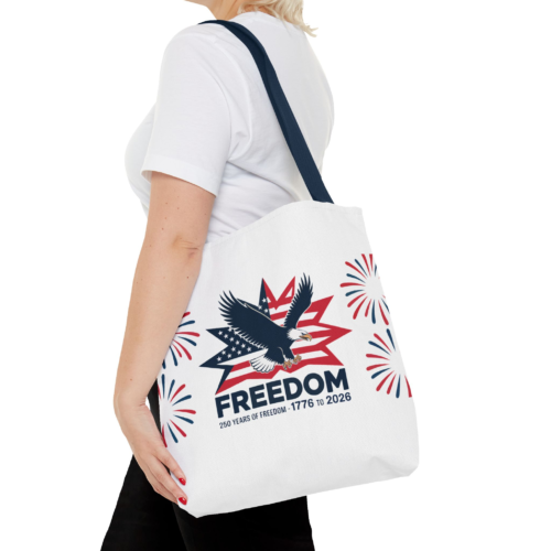 1037367175242540438_2048.webp A person wearing a white t-shirt and black pants has a white tote bag over her shoulder with a patriotic design featuring an eagle, stars, stripes, and the word "FREEDOM" printed on it. The phrase "250 Years of Freedom - 1776 to 2026" is also printed below the word Freedom.