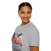 A smiling woman wearing a gray t-shirt with a patriotic design including an American flag, an eagle, fireworks, and the text '1776 Was just the Beginning...'