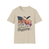 A beige t-shirt featuring a graphic with the American flag, a bald eagle, fireworks, and the text "1776 Was just the Beginning..."