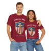 20251124031615-1f0c8e3e-fd95-6c54-a427-664b8ec7a786.webp A man and woman wearing maroon T-shirts with a shield design featuring an American flag pattern, a gold cross, stars, and the text 'God is our shield' and '250th Anniversary'.