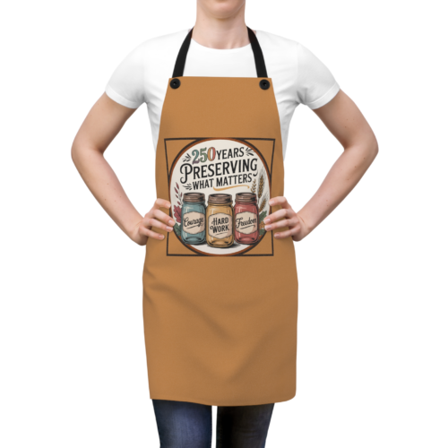 7891221848806255090_2048.webp A person wearing a tan apron with a design of three mason jars labeled 'Courage,' 'Hard Work,' and 'Freedom,' surrounded by the words '250 Years Preserving What Matters'.